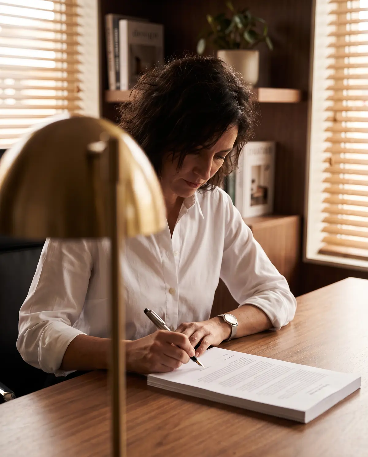 Una mujer firma un documento impreso en su escritorio.